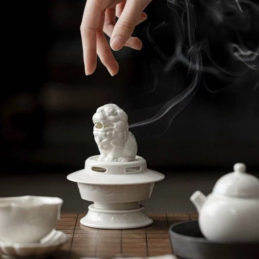 Close-up of white ceramic guardian lion incense burner with smoke curling from the mouth, placed on a wooden tea table
