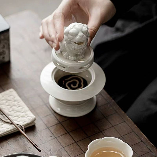 Hand placing the lid of a white ceramic Suanni lion incense burner on a coiled incense disc during use
