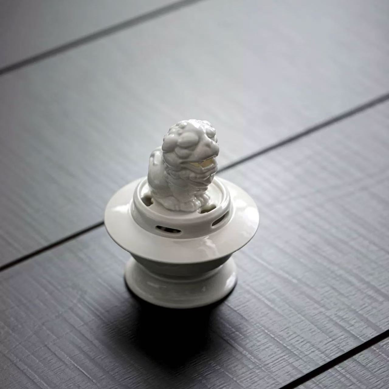 White guardian lion ceramic incense burner placed on a black textured surface, viewed from above