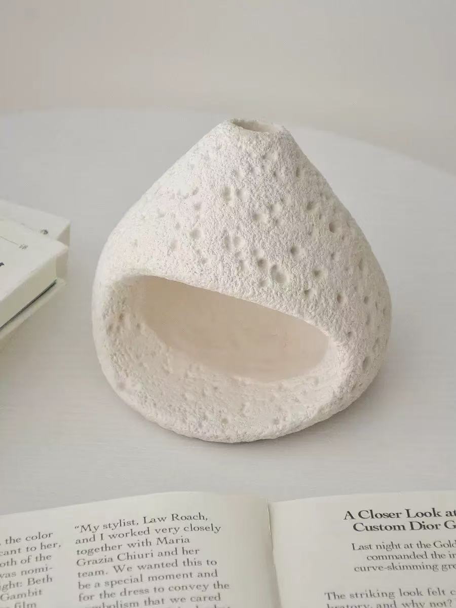 Natural white stone incense burner with porous surface texture, placed on an open book and neutral-toned background in a clean minimalist setting