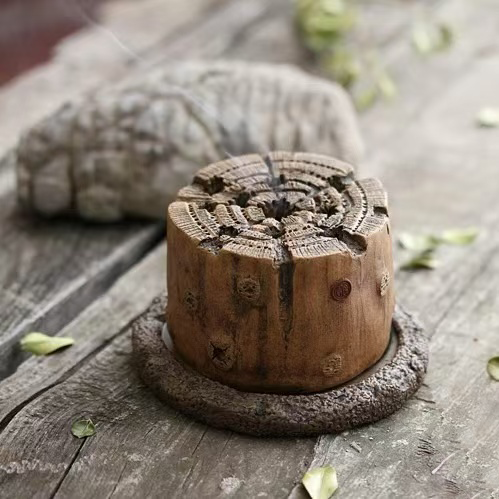 Hand-carved wood-stump incense burner placed on rustic wooden surface, surrounded by scattered leaves
