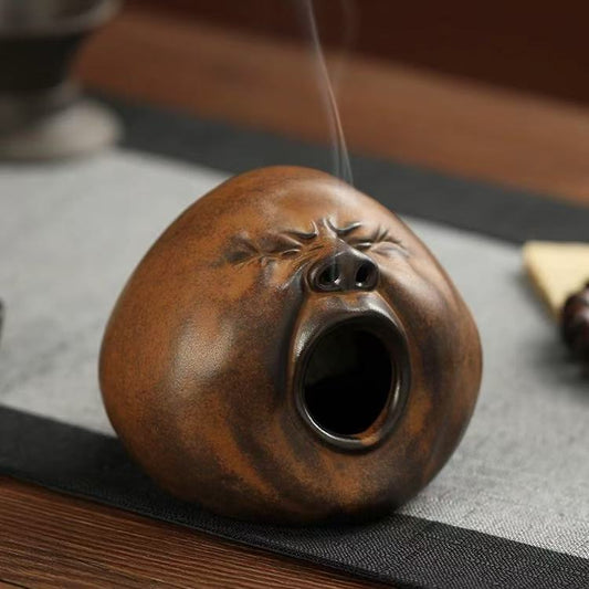 Ceramic incense burner with yawning face design and smoke flowing from the nose and mouth